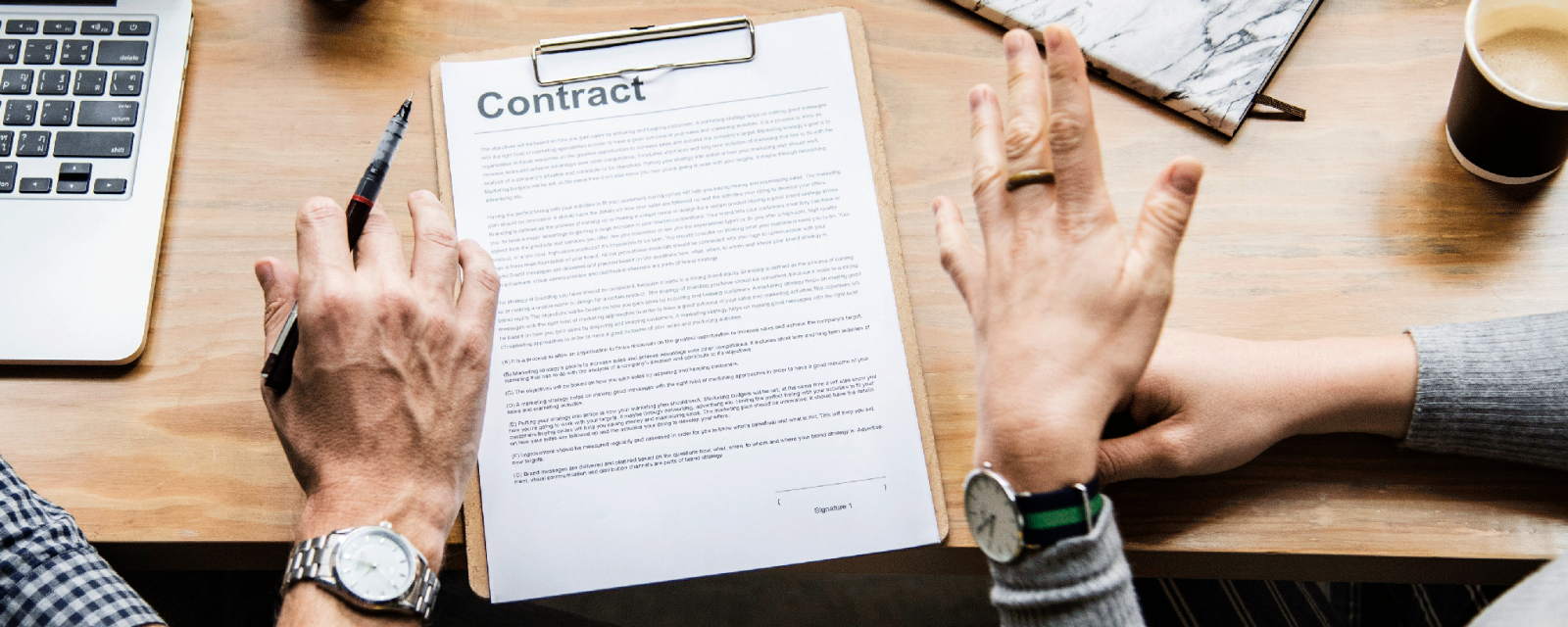 Imagem de um contrato sobre uma mesa com mãos de duas pessoas gesticulando em sinal de acordo
