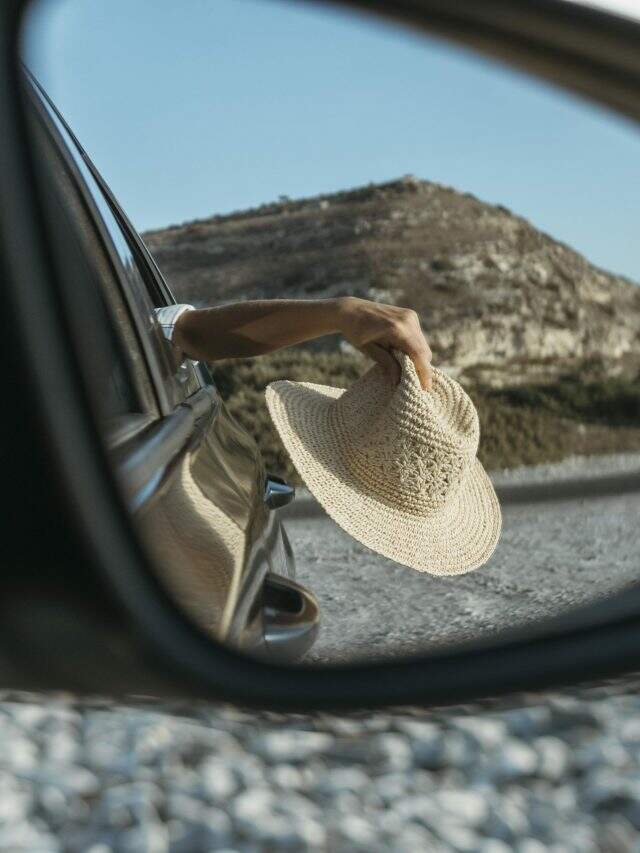 woman-holding-hat-out-window-car-mirror-view